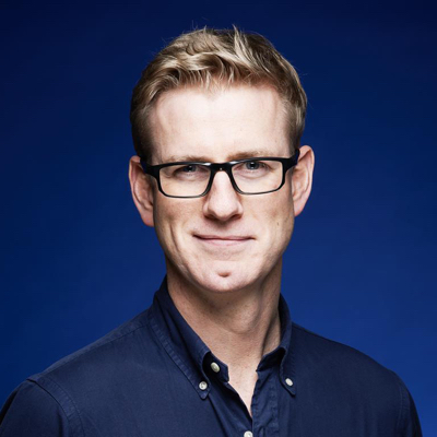 David McClelland smiling at the camera in front of a blue background.